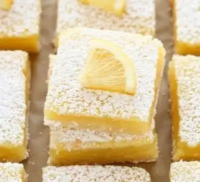 Delicious classic lemon bars topped with powdered sugar on a white plate